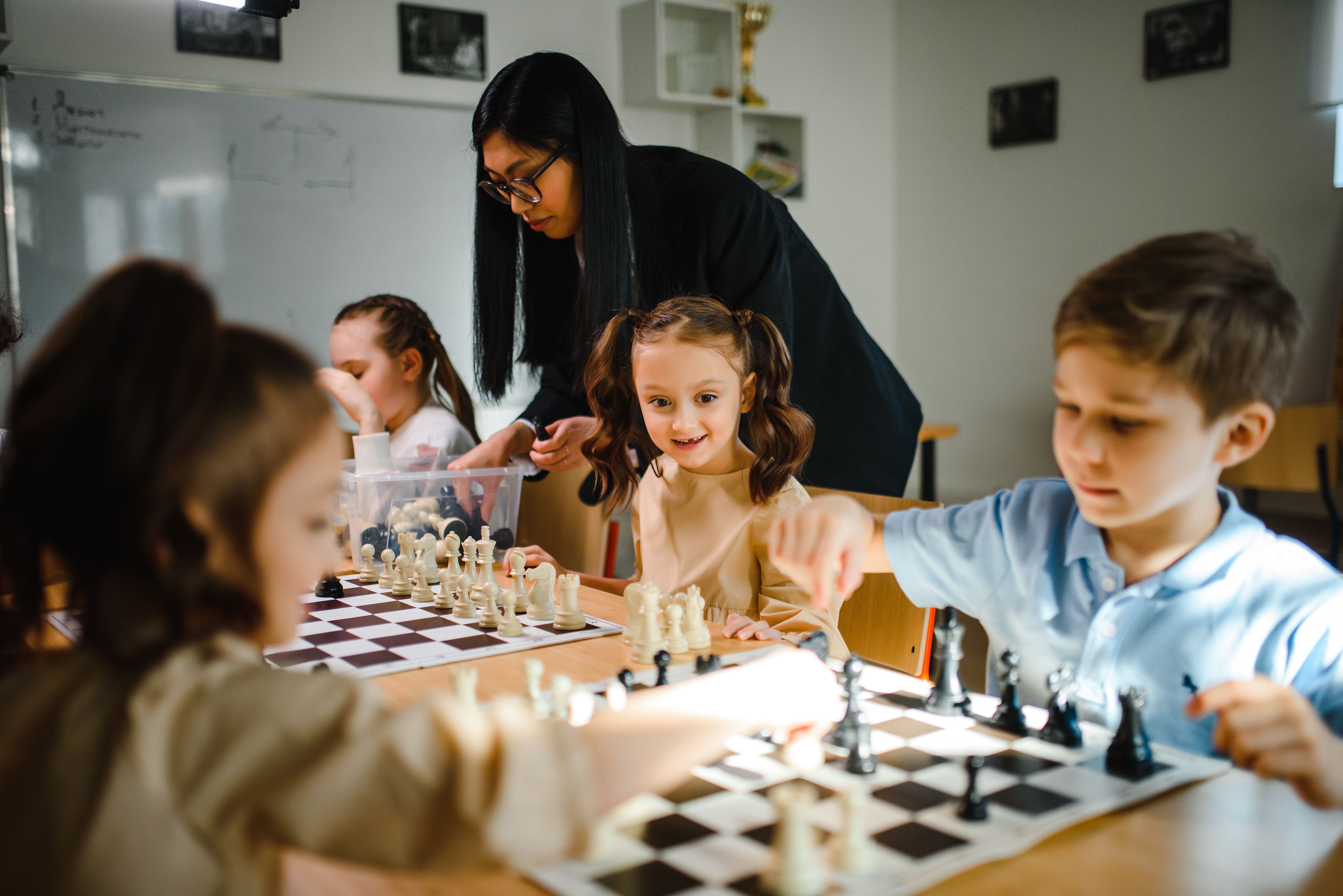 Children playing chess at after school club with teacher supervising — structured activities assessed during Ofsted after school club inspections